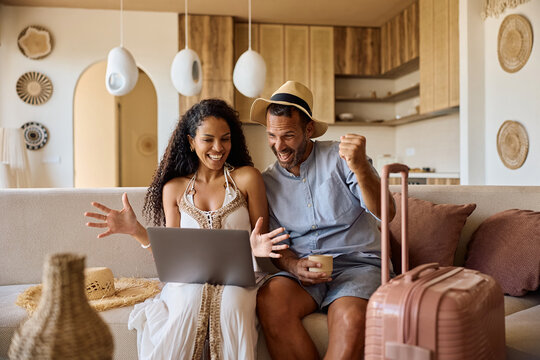 Cheerful couple having fun while using laptop and making plans for their summer vacation.