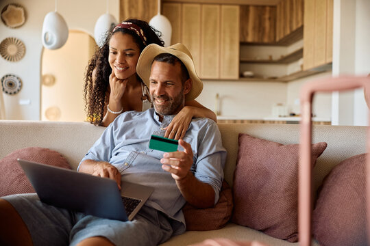 Happy couple using credit card and laptop while making online summer vacation reservation.