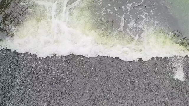 Top view of river water current flowing into a calm lake with white foam.