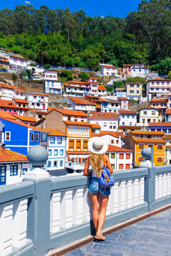 woman tourist with straw hat looking at colorful houses in the historic coastal village of Cudillero, Asturias in Spain