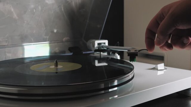 Hand placing stylus on vinyl record and starting turntable, playing LP record with analog HiFi audio system at home.