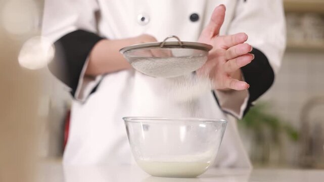 Pastry chef baker hand sift flour through a metal sieve into mixing white glass bowl to aerate for sponge cake batter, preparing dough for baking, culinary preparation recipes, food blogs in kitchen