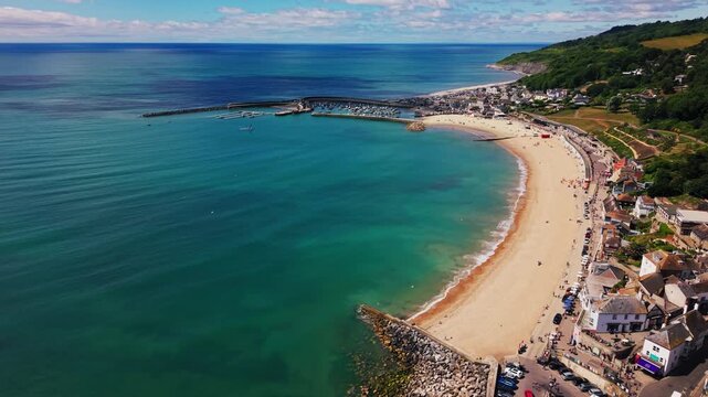 Drone view over a scenic British seaside town with a sandy beach, harbour, marina, turquoise water and busy summer coastline. A bright coastal travel scene useful for tourism, holidays