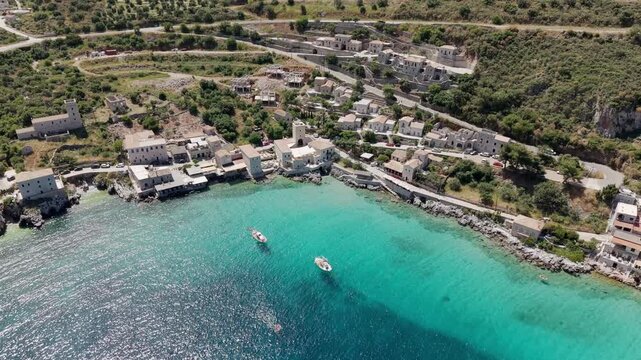 Aerial pullback shot of coastal fishing village Limeni on Mani peninsula, Turquoise waterfront old stone house towers on steep lush green mountains on a sunny day