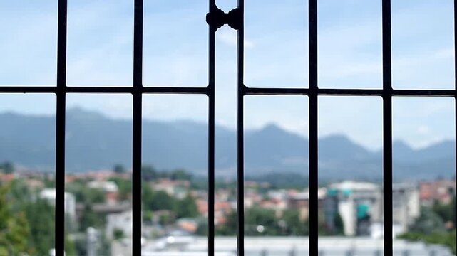 Window static shot with grate overlooking a bright out-of-focus cityscape and mountains background