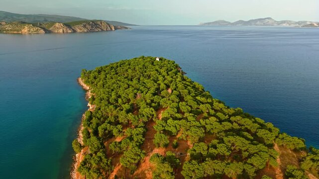 Slow aerial pull-away over the evergreen tip peninsula of Ermioni, tracking backward to reveal a traditional Greek port town, terracotta roofs, and clear blue Argolis Gulf