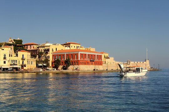 Scenic view of the historic Venetian harbor in Chania, Crete, Greece, with traditional waterfront buildings and boats on the water.