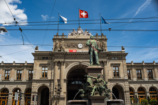 Zurich, Switzerland, June 4, 2026 - Alfred Escher statue and fountain in front of the main railway station facade with flying flags