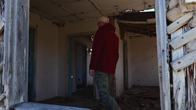 A man explores the interior of an abandoned and dilapidated house on a deserted farm on a cool sunny day