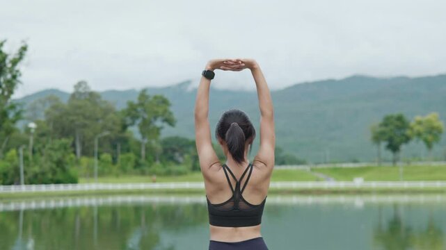Female runner stretching her arms after exercise by a scenic lake, representing cool down routine, flexibility, fitness recovery, wellness and healthy lifestyle.