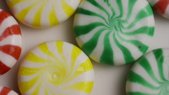 Assorted colorful swirl candies arranged on a white surface slowly drifting past the camera in a cinematic studio shot