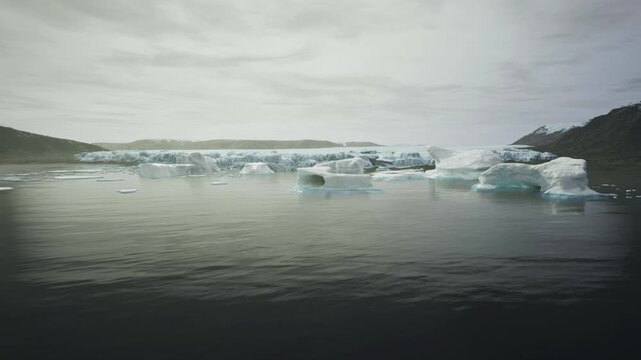 Alaska winter inlet with scattered bergs muted gray palette heavy clouds flat calm water dotted with ice hummocks melancholic atmosphere suggesting seasonal