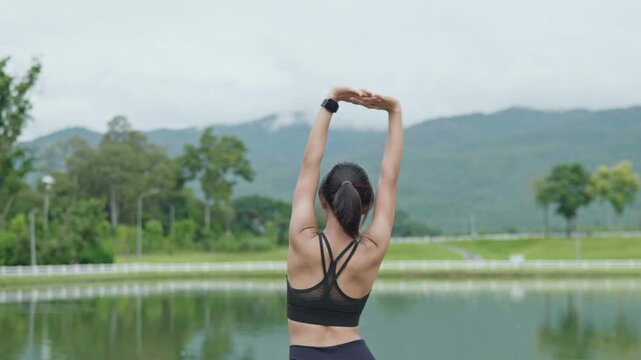Female runner stretching her arms after exercise by a scenic lake, representing cool down routine, flexibility, fitness recovery, wellness and healthy lifestyle.