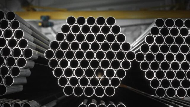 Stacked round steel pipes inside industrial warehouse with symmetrical circular end pattern, high-contrast rim light, repeating metal texture, strong depth, and orderly storage for manufacturing