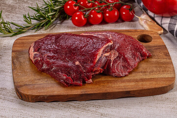 Fototapeta premium Raw beef cheek on wooden cutting board with cherry tomatoes and rosemary