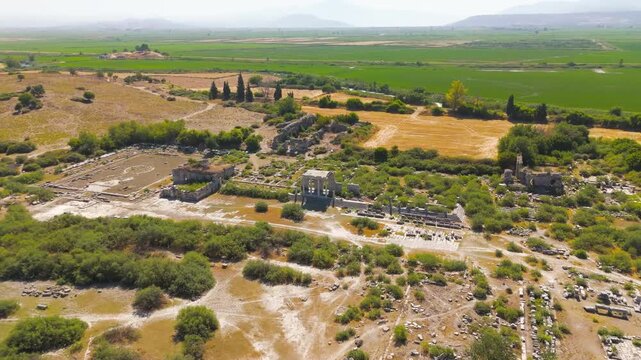 Balat, Turkey. Aerial view over the ancient ruins of Miletus, revealing the North Agora, Bouleuterion council house, and Nymphaeum amid sun-bleached stone and lush green fields. Aerial View, Departur