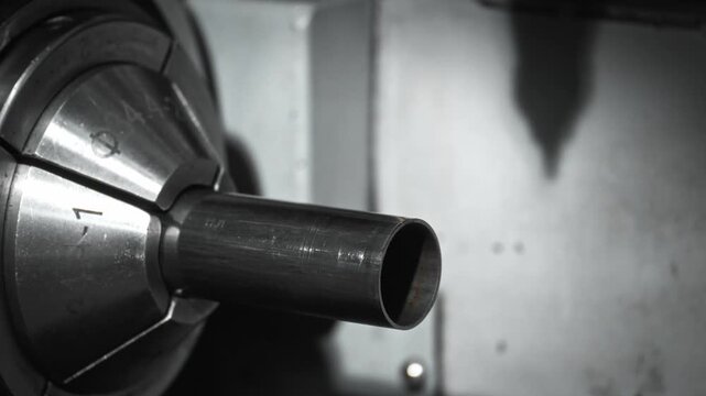 Precision laser cutting steel pipe on rotating chuck, bright sparks falling from nozzle as molten metal glows on polished surface in industrial fabrication workshop