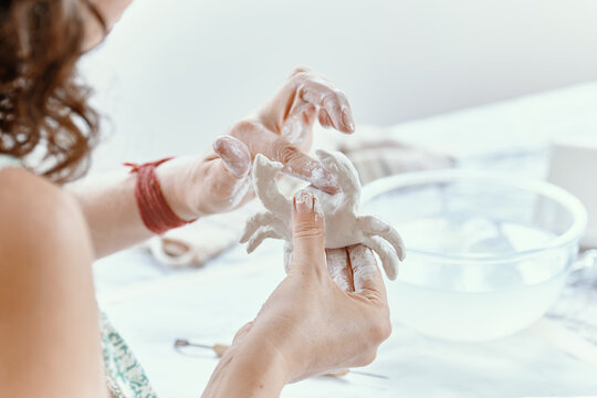 Focused young woman modeling small clay sculpture at table in her art studio. Creative hobby and handmade pottery concept.