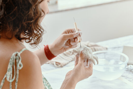 Close up of woman sculpting details on clay figure with metal scraper tool in art studio. Handmade pottery hobby concept.