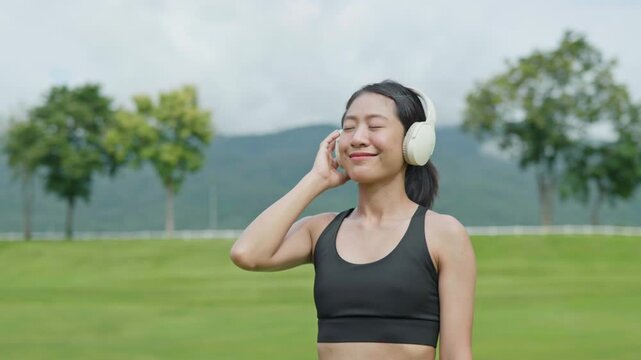 Female runner wearing headphones and listening to music outdoors in a park, representing fitness lifestyle, relaxation, wellness, motivation and active living.