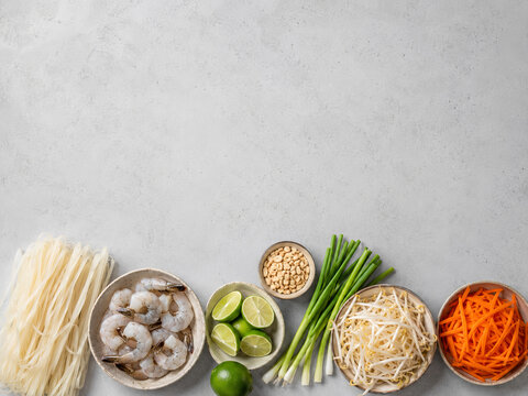 Variedad de ingredientes frescos para preparar un plato de fideos con camarones en una mesa con superficie clara