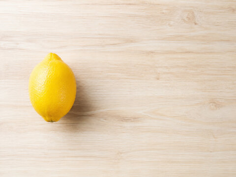 Un lim&oacute;n amarillo sobre una mesa de madera clara en un entorno natural, listos para ser usados en la cocina o en bebidas refrescantes