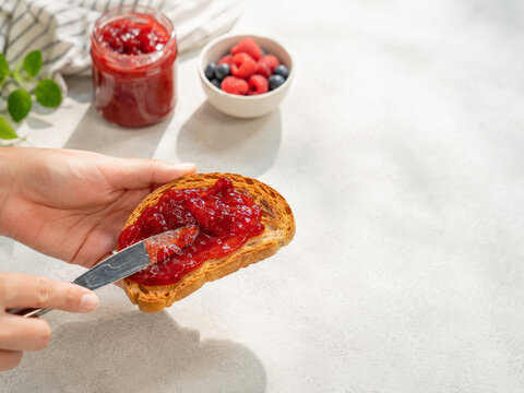 Pan tostado con mermelada en una mesa, acompa&ntilde;ado de frutas y un frasco con m&aacute;s mermelada, mostrando un momento de preparaci&oacute;n y disfrute