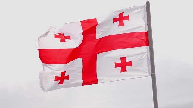 Georgian national flag with its five red crosses waving in slow motion on a flagpole against an overcast sky, representing a symbol of the country's patriotism and freedom slow motion