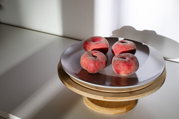 Four ripe saturn peaches on a plate placed on a wooden stand. High contrast dramatic shadows on a white background. ©  Tsvyk L.
