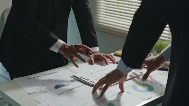 Close-up of colleagues analyzing business charts and financial documents together, representing teamwork, data analysis, planning, strategy and corporate collaboration.