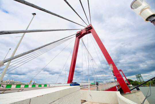 Low-angle view of the iconic red Erasmus Bridge with dramatic clouds, highlighting its cable-stayed design and modern architecture.