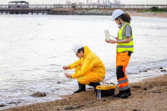 Environmental scientists collecting water samples at the beach near industrial port, Researchers in protective gear testing water quality at the seaside for environmental study