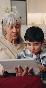 Grandmother, child and relax in home with tablet, browsing and download ebook for education. Senior woman, rest or kid in lounge with digital, watching video and educational games for online learning
