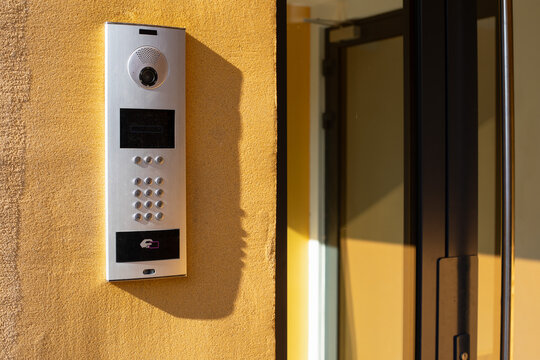 Modern video intercom system with keypad and card reader installed on a yellow wall.