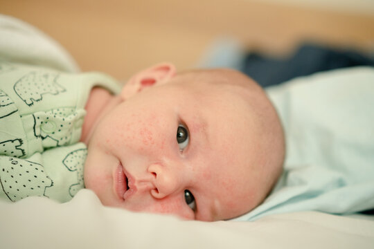 A closeup of a newborn with a gentle expression looking at the camera. The infant resting in soft light presents a peaceful, calm mood that highlights delicate skin in a serene indoor portrait.