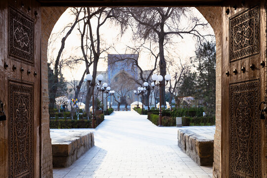 Carved wooden gates framing the pathway to Nadir Divan Begi Madrasah in Bukhara. This atmospheric Uzbekistan landmark scene is ideal for travel publications and cultural heritage projects.