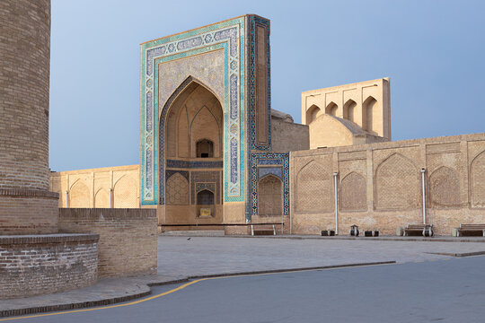 Kalyan Madrasa portal and minaret base on empty Poi Kalyan Square in Bukhara, Uzbekistan. Historic Islamic architecture with turquoise tilework in soft dusk light, ideal for travel and heritage.