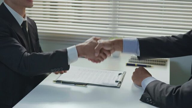 Business partners signing documents and shaking hands in the office, representing agreement, trust, partnership and successful professional collaboration.