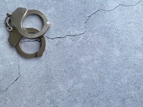 Metal handcuffs on a cracked concrete background symbolizing crime, justice, law enforcement, arrest and criminal investigation with copy space.