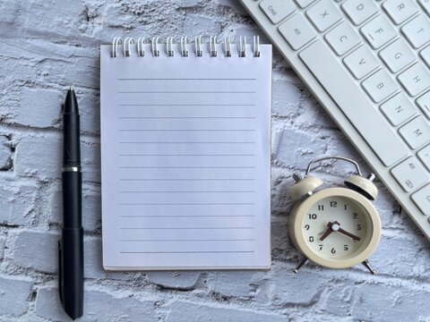 Blank spiral notebook with pen, keyboard and alarm clock on a modern workspace desk for planning, productivity and business concepts.