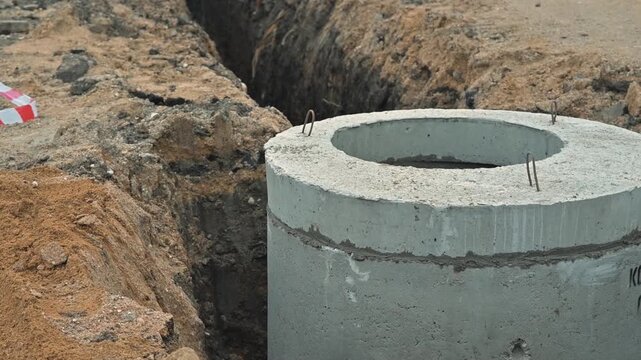 digging a trench to install concrete drainage pipes. The site is busy with machinery and tools, showing the progress of the construction project
