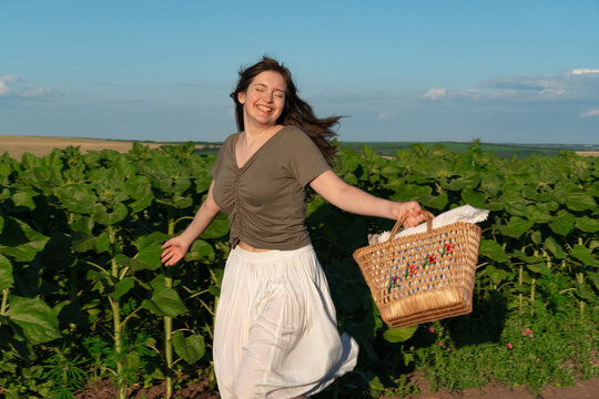 Happy young woman running through sunflower field with wicker basket
