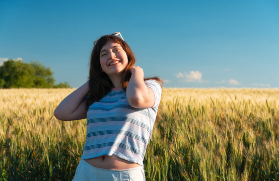 Happy teenage girl smiling in wheat field during summer sunset