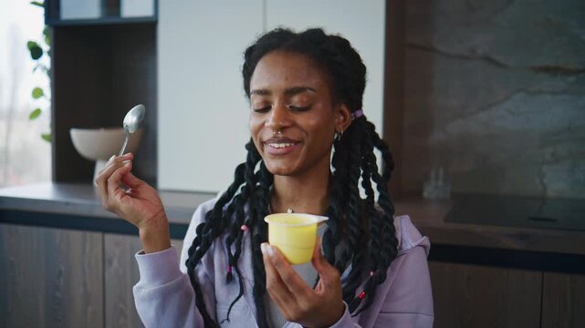 Woman enjoying a snack in a modern kitchen while holding a yellow cup and smiling at the taste at midday