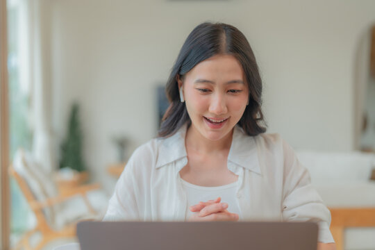 Young Asian woman watching webinar and studying through laptop screen, enjoying e-learning course in a bright home interior.