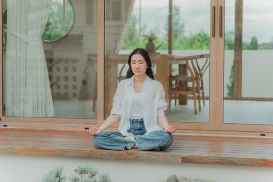 Young Asian woman in morning meditation routine outside vacation home, front view of balanced healthy living and slow life at villa.