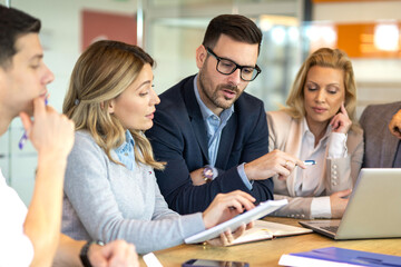 Obraz na płótnie Canvas A manager is pointing at a laptop while colleagues are reviewing notes, showing analysis, planning, leadership and collaborative decision making.