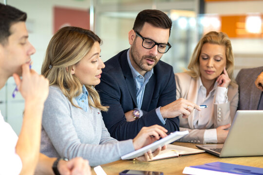 A manager is pointing at a laptop while colleagues are reviewing notes, showing analysis, planning, leadership and collaborative decision making.