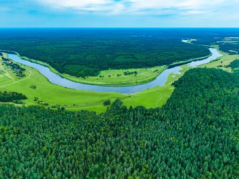 Aerial view of lush green forests and winding river landscape under clear blue sky