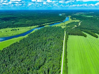 Obraz premium Aerial view of lush green fields and winding river meandering through dense forest landscape